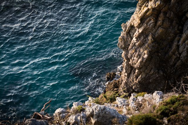 Picture showcases a stunning view of a rugged rocky cliff overhanging clear blue ocean waters. Perfect for uses in travel blogs, environmental campaign material, adventure brochures, and scenic wallpapers.