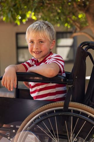 Smiling blond boy in wheelchair outdoors enjoying sunlight and courtyard moments