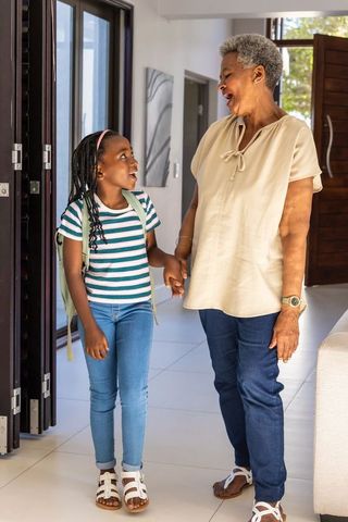 African american grandmother chatting with granddaughter at home entrance holding hands