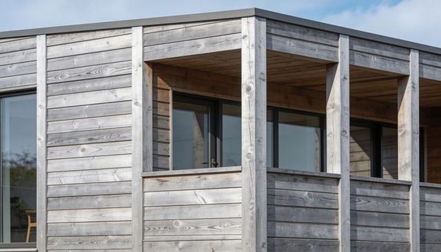 Weathered timber balcony with vertical posts and glass doors on modern wood-clad facade