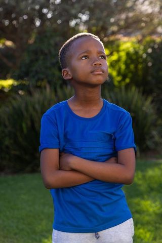 Contemplative african american boy gazing upward in blue shirt backlit garden golden hour