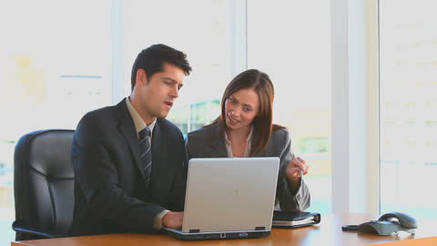 Coworkers Collaborating at Desk with Laptop in Modern Office