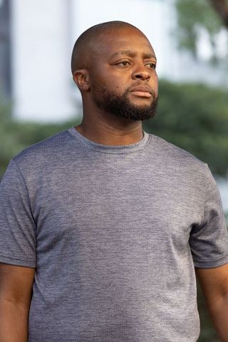 Thoughtful man standing gazing right in urban green courtyard wearing grey heather t-shirt