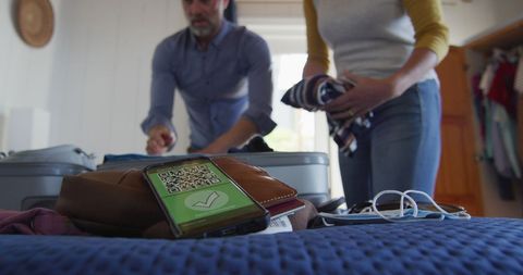 Couple prepping luggage with covid-19 vaccine passport on smartphone hub