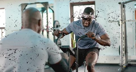 Pushing limits on air bike with coach observing during intense gym training