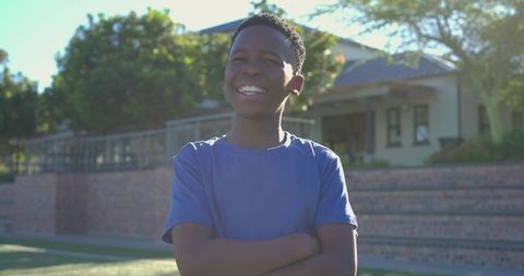 Confident african teen standing arms crossed smiling sunlit suburban yard portrait