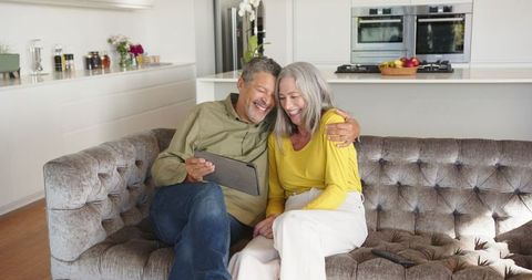 Senior Couple Relaxing on Velvet Sofa with Digital Tablet in Modern Home