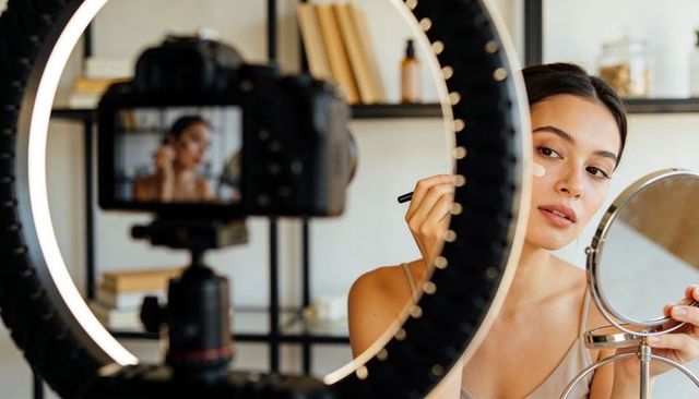 Beauty creator applying makeup on camera with ring light and mirror for tutorial recording