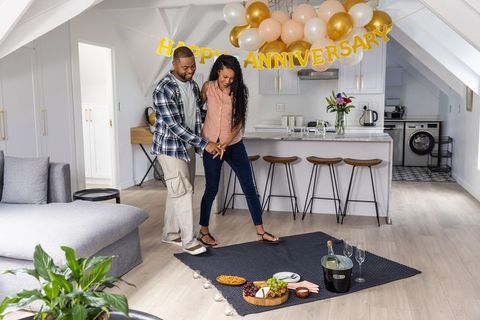 Couple celebrating intimate anniversary at home with picnic blanket, balloons, candles, champagne
