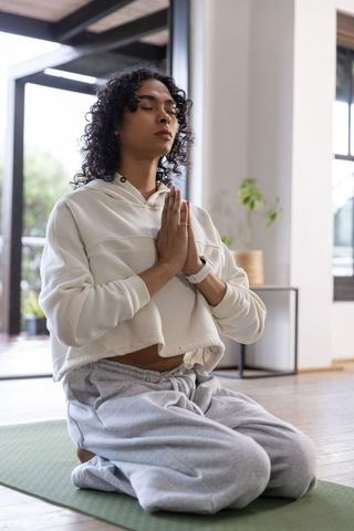 Nonbinary person practicing kneeling meditation at home with smartwatch in minimalist room