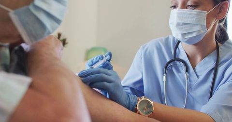 Nurse administering vaccine to patient wearing mask and gloves, close-up clinical injection