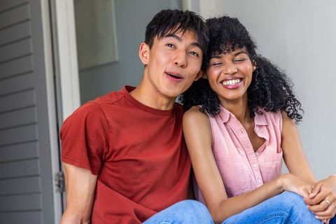Laughing interracial couple relaxing on porch steps sharing surprise and affection