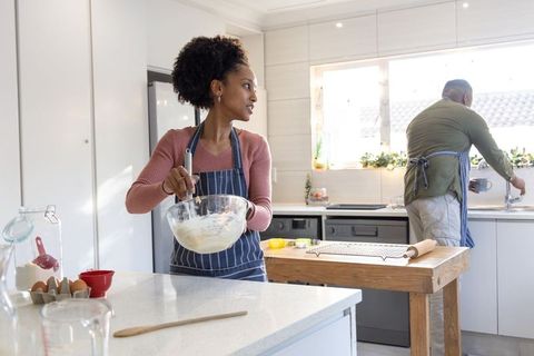 African american couple baking, whisking batter at kitchen island in bright modern kitchen