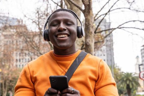 Smiling african american man listening to music outdoors with smartphone and headphones