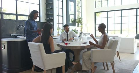 African american friends enjoying drinks at round wooden table in sunlit modern kitchen
