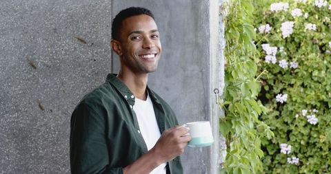 Smiling Young Man Enjoying Coffee Outdoors with Nature Background