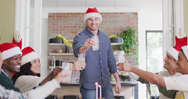 Group of friends gathered in living room during Christmas wearing Santa hats, toasting with glasses of milk. Perfect for holiday-themed advertisements, festive magazine spreads, or social media campaigns focused on holiday gatherings and celebrations.