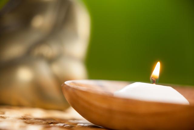Lit candle in wooden bowl on mat
