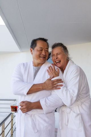 Joyful Senior Couple Relaxing on Balcony in Bathrobes with Tea