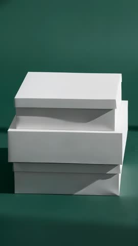 Vertical video showing stacked white boxes rotating and opening lids on green backdrop
