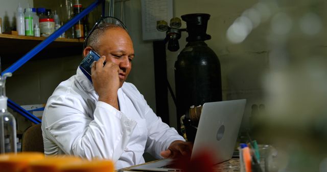 Scientist in lab coat talking on phone working on laptop - Download Free Stock Images Pikwizard.com