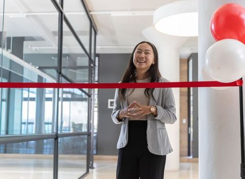 Asian businesswoman smiling during ribbon-cutting ceremony at modern office grand opening