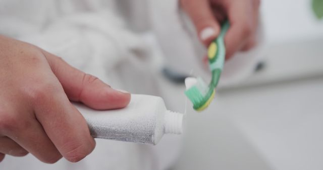 Close-up of person putting toothpaste on green toothbrush in bathroom. Ideal for articles on oral hygiene, dental care tips, and daily self-care routines. Could be used in advertisements for dental products or health websites.