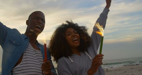 Joyful african american couple celebrating with sparklers at sunset beach