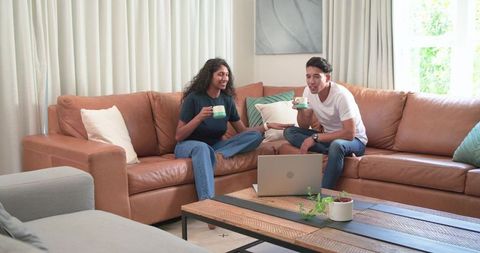 Editor and author collaborating on laptop over coffee in modern living room discussing drafts