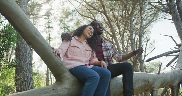 Scene of a happy couple sitting on a tree branch in the forest, smiling and enjoying nature together. Perfect for concepts related to love, bonding, outdoor recreation, and spending quality time in nature.