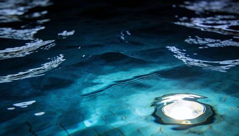 Submerged pool light casting teal ripples over mosaic tile floor for night ambience