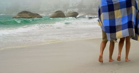 Couple walking on foggy beach under checkered blanket