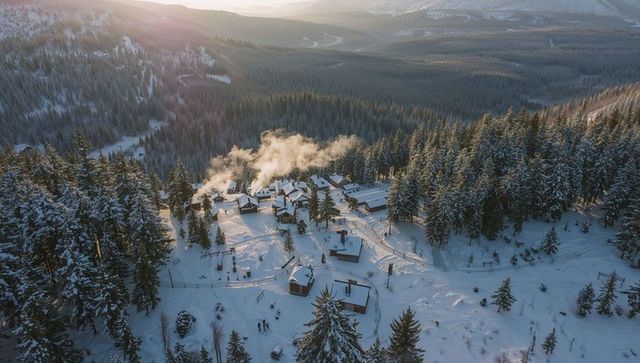 Sunrise Over Snowy Mountain Village with Smoking Chimneys and Forested Aerial Panorama