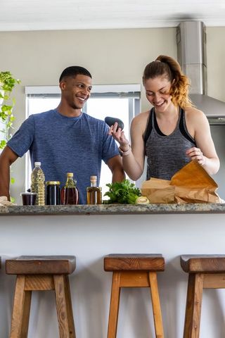 Couple unpacking groceries and using phone ar to identify herbs in modern kitchen