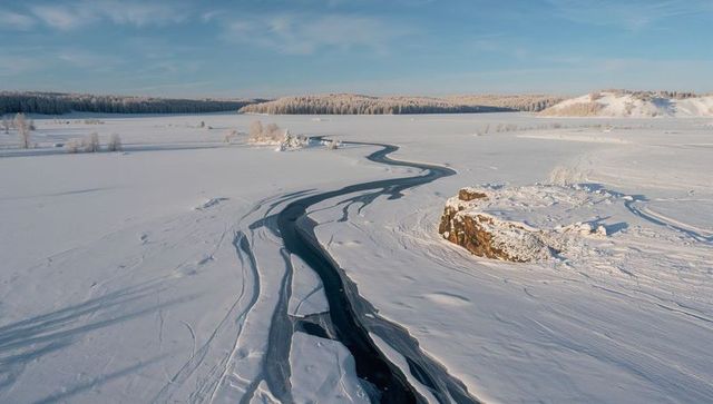 Sinuous ice-fissure cutting through frozen lake toward sunlit rocky outcrop at dawn