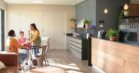 Multicultural friends enjoying coffee while barista serving in modern minimalist cafe