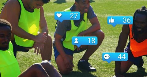 Soccer players resting on sunlit turf wearing neon training bibs with social media icons