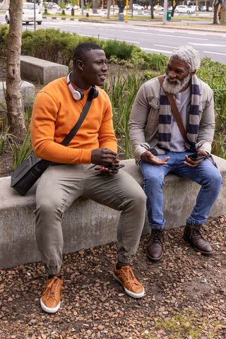 African american multigenerational friends chatting on urban bench with phones and smiles