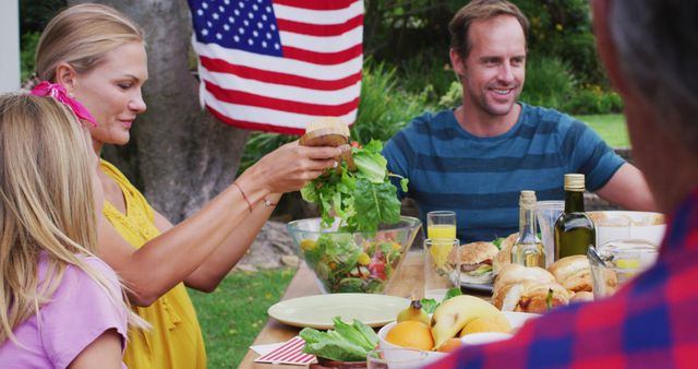 Smiling caucasian couple serving family having celebration meal together in garden. three generation family celebrating independence day eating outdoors together.