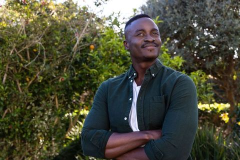 African american man standing arms crossed in sunlit backyard looking up with calm smile