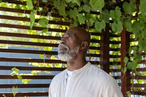 Senior african man gazing upward under vine-covered pergola, peaceful outdoor portrait