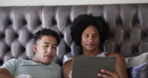 Male couple watching tablet in bed on tufted headboard modern relaxed bedroom lifestyle