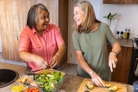 Senior Female Friends Joyfully Preparing Healthy Salad in Kitchen