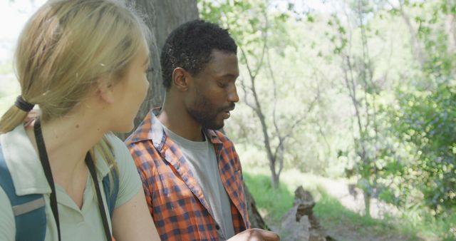 A multiracial couple is enjoying a forest hike, immersed in a conversation while nature surrounds them. Ideal for illustrating themes of outdoor activities, friendship, and adventure. Suitable for travel blogs, promotions for hiking gear, and environmental conservation campaigns.