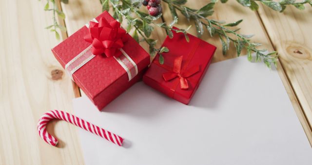 Image shows two red gift boxes with ribbons, a candy cane, a blank letter, and spruce twigs with berries on a wooden background. Perfect for illustrating holiday celebrations, Christmas greetings, winter traditions, and seasonal decorations.