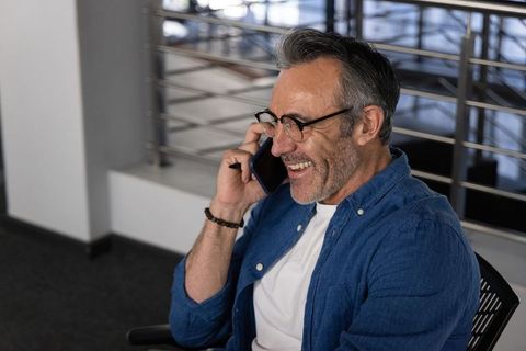 Middle-aged man smiling while talking on smartphone in modern office mezzanine