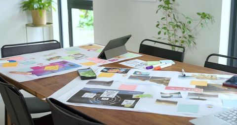 Creative team brainstorming on wooden table with layout sheets, sticky notes, devices