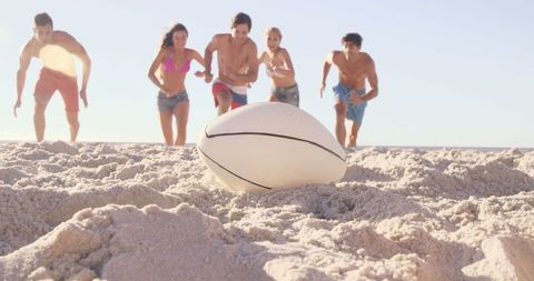 Diverse group running for rugby ball on beach