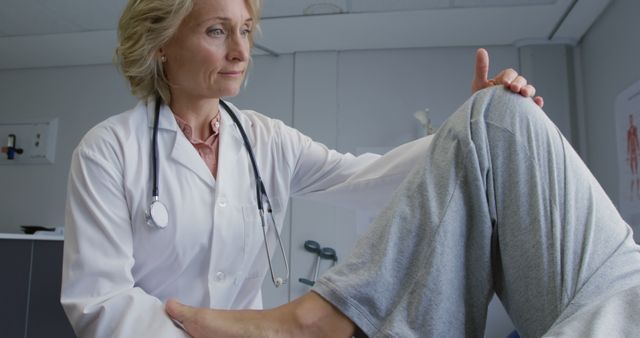 Elderly female doctor examining a patient's knee in a well-lit medical clinic. Suitable for use in healthcare advertisements, medical websites, physiotherapy awareness campaigns, and articles discussing knee injuries and their treatments.