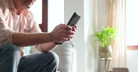 Man Relaxing at Home Holding Smartphone with Coffee Mug Nearby